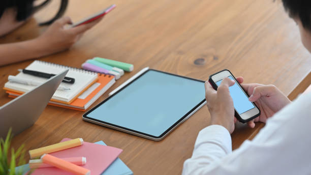 istock Cropped image of website designer team working with computer laptop, tablet, stylus pen and smartphone while sitting together at the wooden working desk over comfortable living room as background. 1218554542