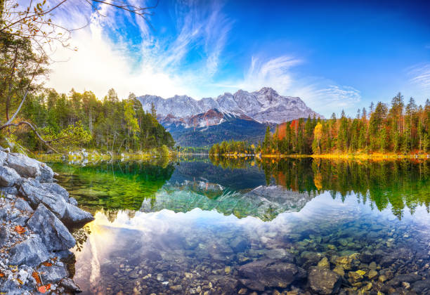 faboulus paesaggio autunnale del lago eibsee di fronte alla cima di zugspitze sotto la luce del sole. - zugspitze mountain lake autumn germany foto e immagini stock