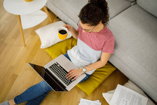 istock Young woman sitting on floor at home working with laptop and documents 1218558149