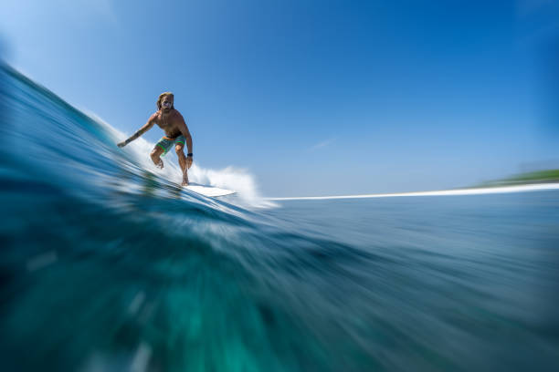 長い髪を持つ若い男のサーファーは、モルディブで速く、完璧な海の波をサーフィン - splashing maldives human hair spray ストックフォトと画像