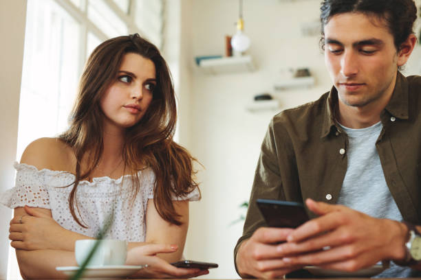 Woman feeling ignored on a date Woman looking unhappy while her man paying no attention to her and busy using his mobile phone. Sulking woman sitting next to man reading text messages during a date. indifference stock pictures, royalty-free photos & images