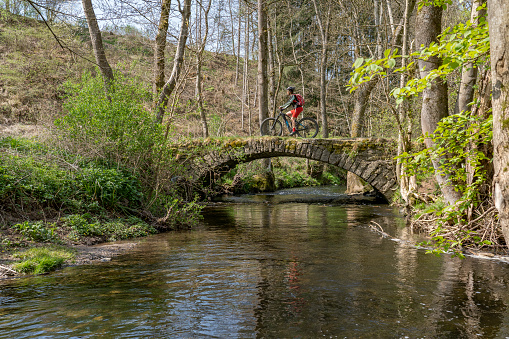 pretty mid age woman riding her electric mountain bike at a little river on a warm sunny spring day