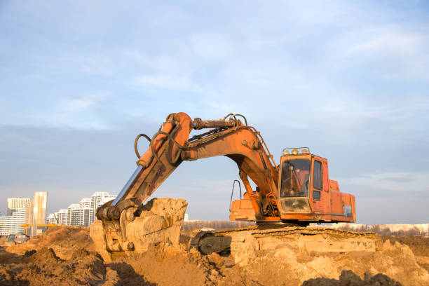 istock Excavator at earthworks on construction site. Backhoe loader digs a pit for the construction of the foundation. Digging trench for laying sewer pipes drainage in ground. Earth-Moving Heavy Equipment 1218568281