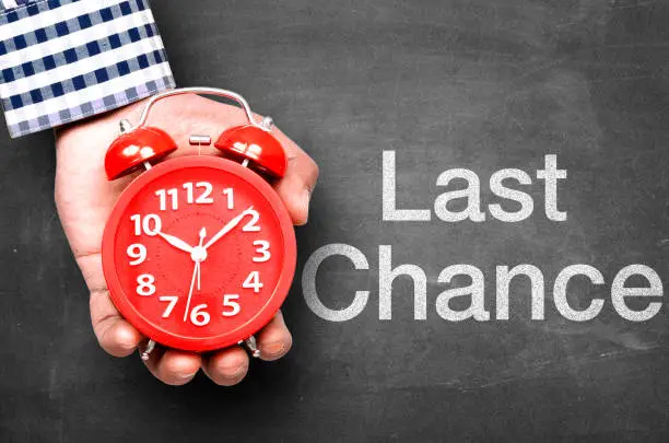 Last chance message on blackboard with hand holding alarm clock