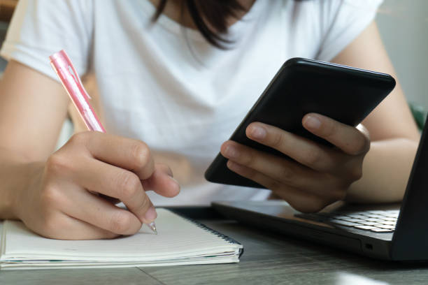 istock Young business woman sitting at table with laptop and taking notes in notebook. 1218578853
