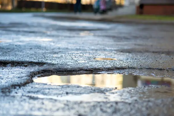 Photo of Close up of a road in very bad condition with big potholes full of dirty rain water pools.