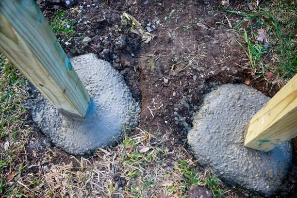 Building fence in progress: setting up wooden poles in concrete foundation.