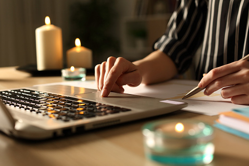 Close up of entrepreneur woman hands working during power outage with candles sitting on a desk at home office in the night