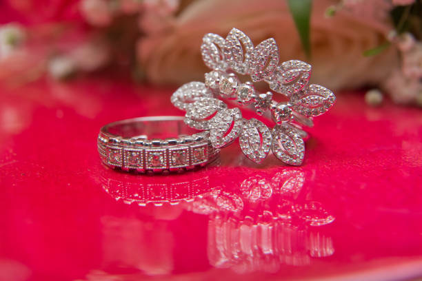 istock White wedding rings . flower bouquet selective focuse .Two silver wedding rings red background . Romantic and lovely wedding , macro . Bride and groom with Engagement gold rings put on the red table . 1218588134