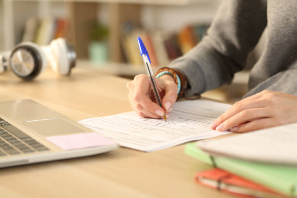 Student hands filling out form document at home Close up of student girl hands filling out form document sitting on a desk at home exam student university writing stock pictures, royalty-free photos & images