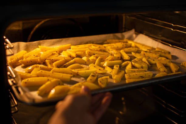 hand putting tablett mit geschnittenen kartoffeln in den ofen, um eine gesunde hausgemachte pommes frites zu machen. - french fries fast food french fries raw raw potato stock-fotos und bilder
