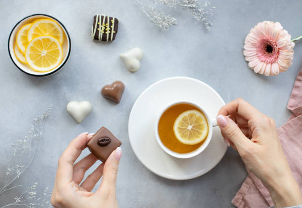 ręce młodej kobiety z ciemnymi cukierkami czekoladowymi i białą filiżanką herbaty na szarym tle. - afternoon tea tea women table zdjęcia i obrazy z banku zdjęć