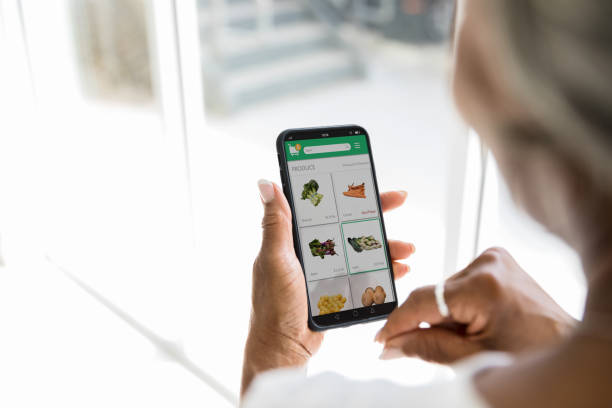 Woman uses grocery delivery app A woman uses a grocery delivery app on her smartphone. She is selecting fresh produce while using the app. ordering stock pictures, royalty-free photos & images