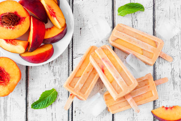 Summer peach yogurt popsicles, top view table scene against white wood Summer peach yogurt popsicles, top view table scene against a rustic white wood background flavored ice photos stock pictures, royalty-free photos & images