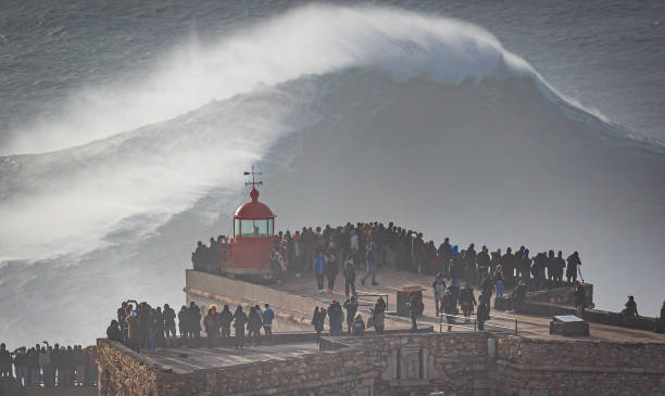 Biggest Wave In The World, Nazare, Portugal Stunning Image of giant wave crashing into cliff and lighthouse after major Atantic Storm. nazare surf stock pictures, royalty-free photos & images
