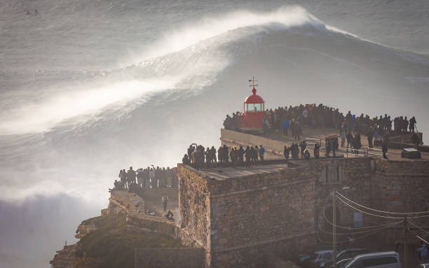 Biggest Wave In The World, Nazare, Portugal Stunning Image of giant wave crashing into cliff and lighthouse in Golden Light, after major Atantic Storm. nazare surf stock pictures, royalty-free photos & images