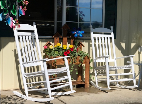 Three white Adirondack chairs overlook a Springtime garden blooming with yellow daffodils.