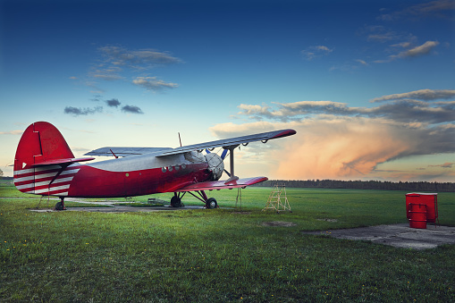 Old red biplane on a green field at sunset