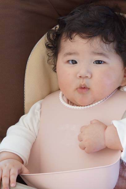 bebé de 5 meses de edad sentado en una silla de bebé después de comer comida para bebés. - 0 1 mes fotografías e imágenes de stock