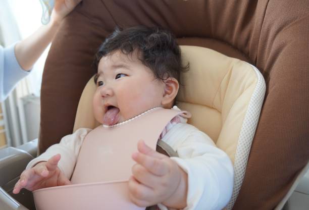 bebé de 5 meses de edad sentado en una silla de bebé después de comer comida para bebés. - 0 1 mes fotografías e imágenes de stock