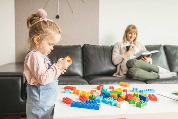 istock Mother reading a book and her daughter playing with toy bricks 1218608502