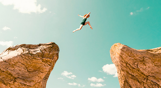 Concept of determination, adrenaline and over coming fear. Woman jumps from one rock formation to another. It is a dangerous jump and she uses all of her speed and strenght to make it across.