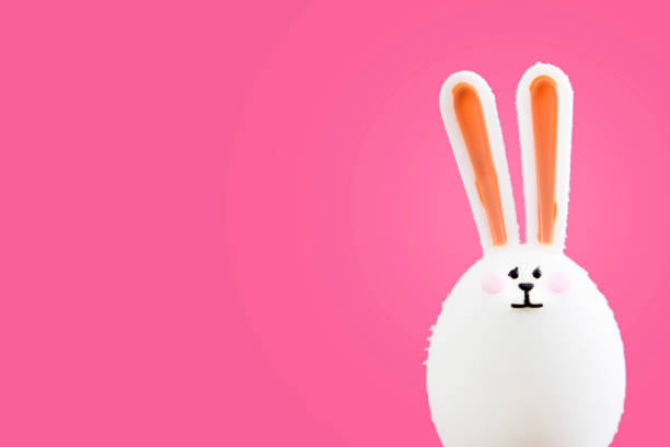istock Funny toy Easter bunny with ears in the shape of an Easter egg isolated on a pink background. Easter concept. Copy space 1218614019