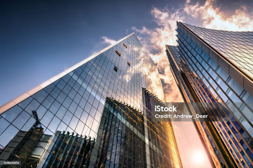 Looking up a reflections on glass covered corporate building Low angle view of tall corporate glass skyscrapers reflecting a blue sky with white clouds Building Exterior Stock Photo