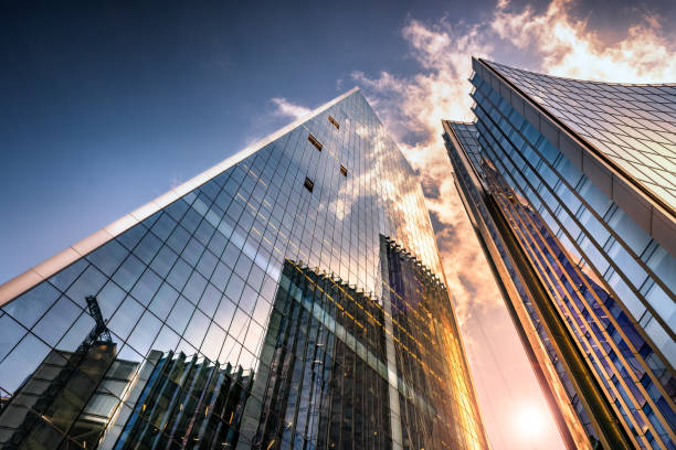 Looking up a reflections on glass covered corporate building Low angle view of tall corporate glass skyscrapers reflecting a blue sky with white clouds directly below stock pictures, royalty-free photos & images