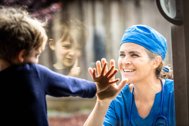 travailleur de soins de santé mature posant voyant son fils avec un verre de fenêtre les séparant pour éviter la contagion possible - son photos et images de collection