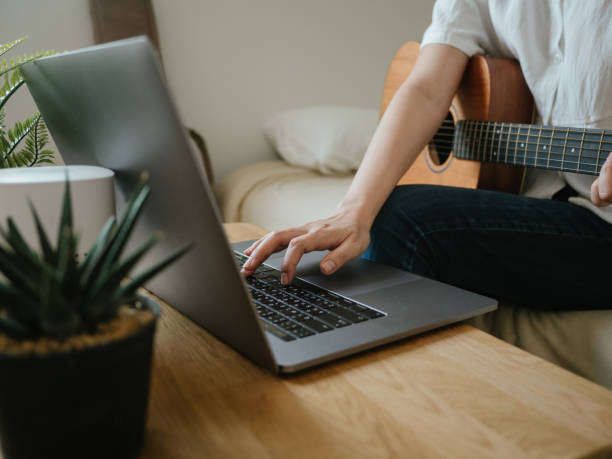 istock Young woman using laptop to video chat while playing acoustic guitar 1218618086