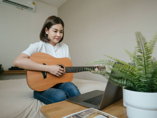 istock Young woman using laptop to video chat while playing acoustic guitar 1218618096