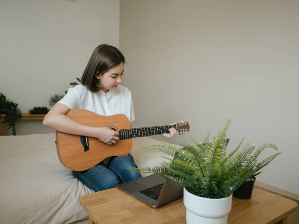 istock Young woman using laptop to video chat while playing acoustic guitar 1218618177