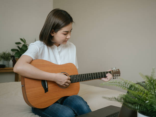 istock Young woman using laptop to video chat while playing acoustic guitar 1218618179