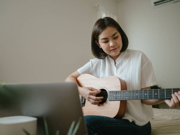 istock Young woman using laptop to video chat while playing acoustic guitar 1218618198