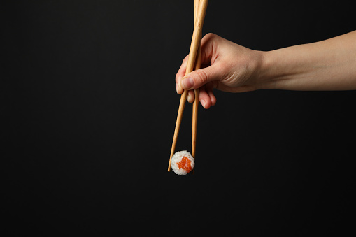 Female hand with chopsticks hold sushi roll on black background. Japanese food