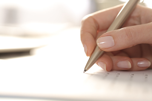 Woman hand filling out form with pen on a desk