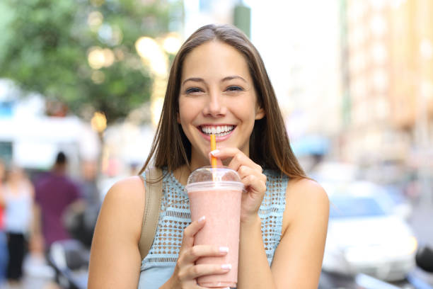 ragazza felice che ti guarda bevendo frullato per strada - smoothie drinking women drink foto e immagini stock