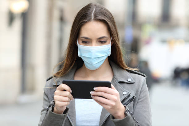 istock Woman with mask watching video on phone 1218621221