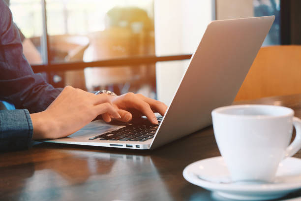 Primo piano di giovani uomini d'affari che lavorano da remoto con laptop e caffè per computer a casa durante la diffusione della pandemia Covid-19 e Coronavirus, auto quarantena e lavoro da casa - foto stock