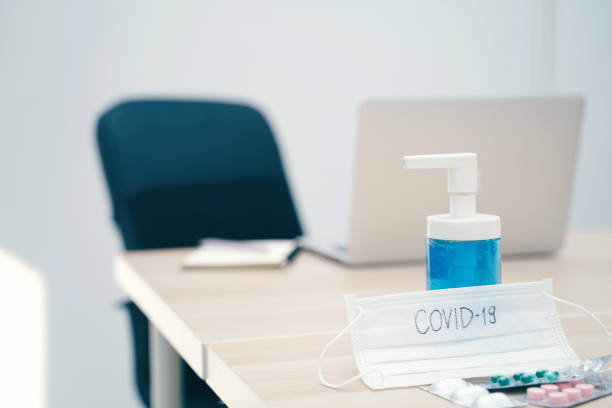 Scrivania workspace di laptop per computer con gel e maschera disinfettante per l'alcol con testo covid-19 e medicina per prevenire la diffusione della pandemia Covid-19 e Coronavirus, lavoro da casa e concetto di igiene - foto stock