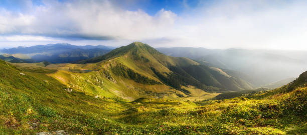 Wonderful springtime panoramic landscape in mountains at sunrise. Grassy slopes and forested hills illuminated with morning sunshine. Wild scenery. Farcau Peak. Maramures. Romania. Europe. Wonderful springtime panoramic landscape in mountains at sunrise. Grassy slopes and forested hills illuminated with morning sunshine. Wild scenery. Vinderel Lake and Farcau Peak. Mountain Maramures Nature Park. Natural reserve. Carpathians. Romania. Europe. Concept ecology protection. maramureș stock pictures, royalty-free photos & images