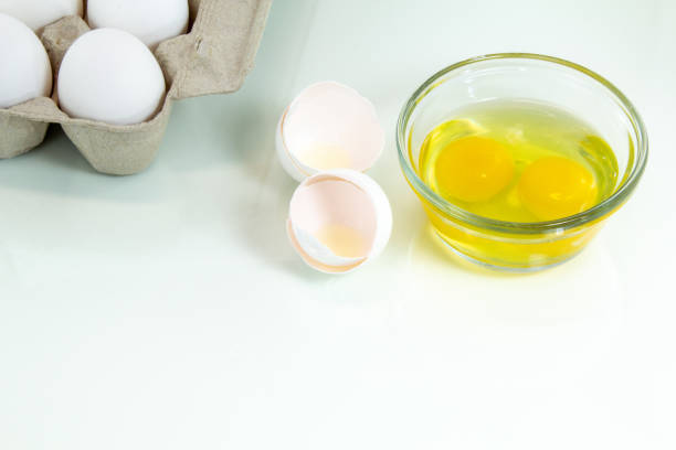 istock Two broken eggs in a glass bowl with a carton of whole white eggs. White background. 1218626507