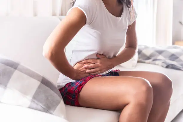 Photo of Woman sitting on a couch at home holding her appendix in a stomach ache.