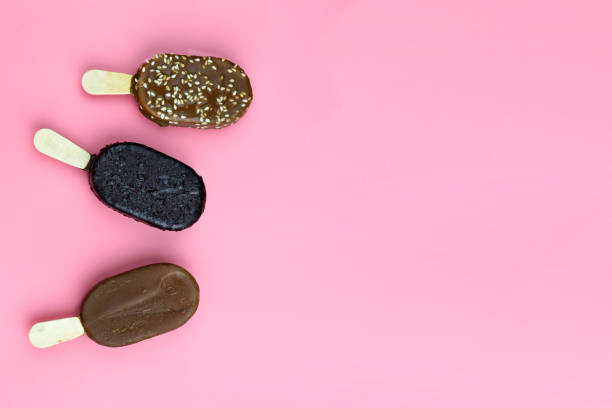 Ice cream sticks with chocolate, roasted almonds and sesame on pink background. Top view. Copy space. Pattern