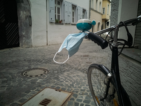 Bicicleta con máscara médica de protección facial colgando en el viento en la barra de dirección en callejón completamente vacío del casco antiguo en Ratisbona, Baviera, Alemania el lunes de Pascua 2020 durante el bloqueo de pandemia del virus Corona photo