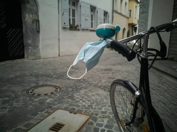 Bicycle with medical face protection mask dangling in the wind on steering rod in completely empty alley of old town in Regensburg, Bavaria, Germany on Easter Monday 2020 during Corona virus pandemic lockdown