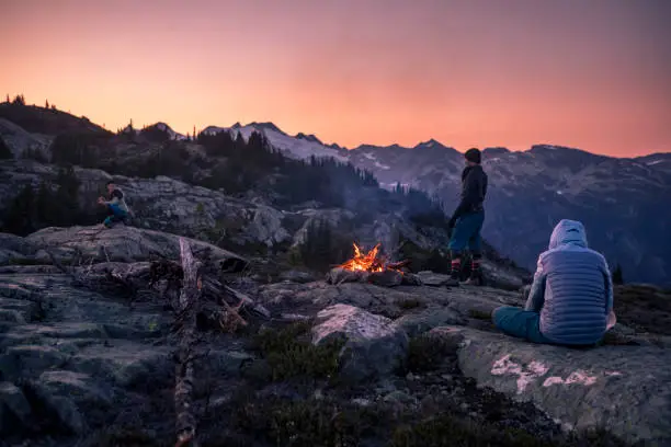 Photo of Friends near campfire on top of mountain at dusk.