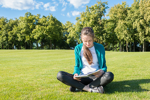 University student reading a book in the park on a sunny summer day. Concept - Education and knowledge.