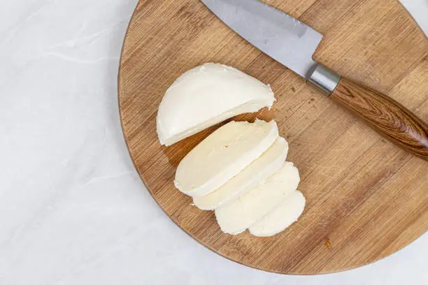 Sliced Mozarella cheese on the round wooden board.